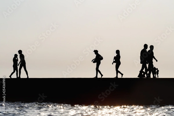 Fototapeta Silhouettes of people having a rest on a pier on the seashore. Rest on the sea beach.