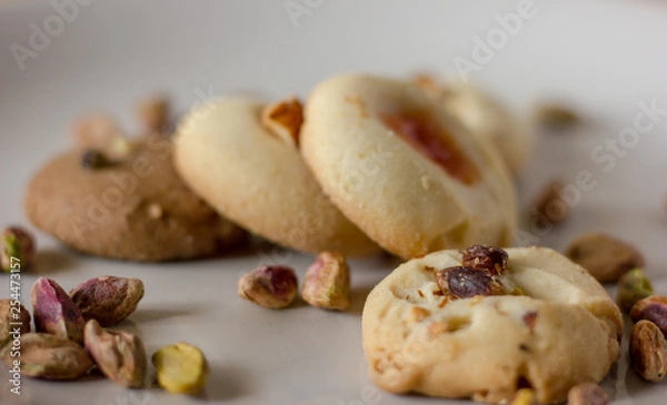 Fototapeta Pistachio butter cookies oven fresh with vanilla and chocolate base close up, with pistachios sprinkled in  on top of them isolated in a white background. 
