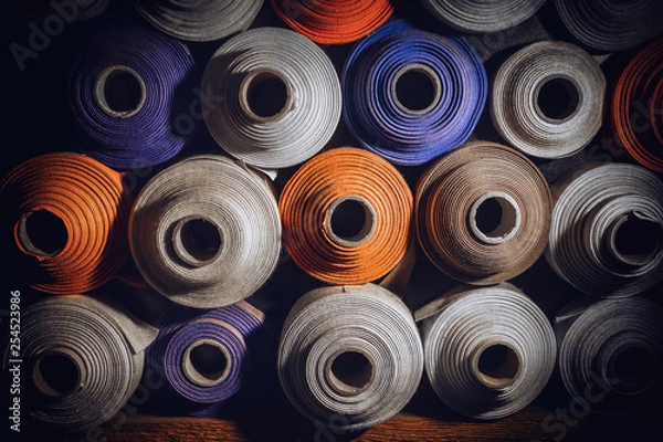 Fototapeta many textile rolls of blue, white and orange colors stacked one over the other in dark light