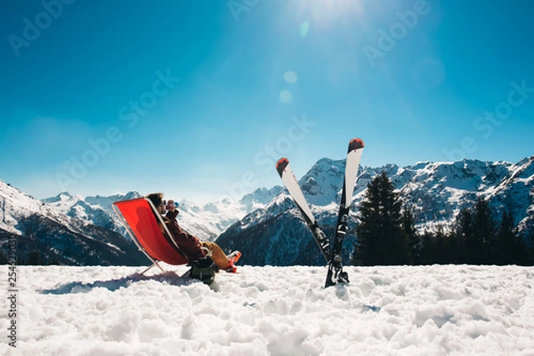 Fototapeta guy chilling out on the slope after skiing in Aprica ski resort with his skies next to him