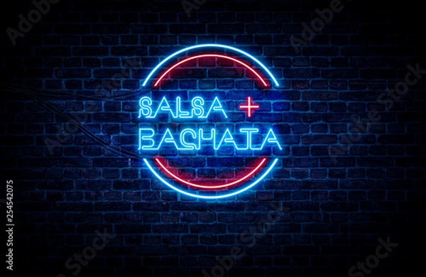 Fototapeta Salsa and Bachata written on a red and blue neon sign, with a brick wall in the background.