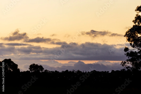 Fototapeta Rolling cloudscape over silhouette horizon at dusk.