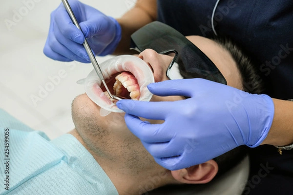 Fototapeta A female dentist examines the oral cavity of the patient with a tool with a mirror. Close-up portrait of a patient with a mouth open, a doctor in gloves holds a dental mirror.