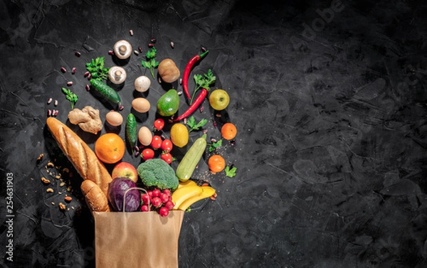 Fototapeta Healthy food in full paper bag of different products vegetables and fruits on dark background