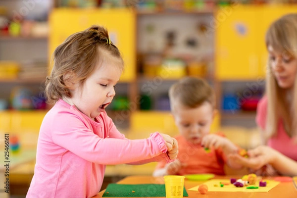 Fototapeta Nurdery babies playing with play clay in kindergarten or playschool