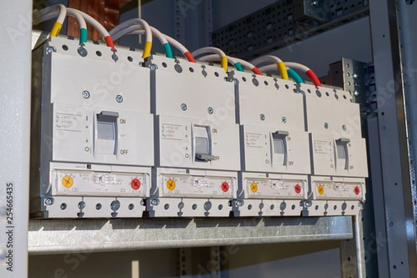 Obraz Four powerful industrial circuit breakers are fixed in the electrical Cabinet in line. Modern and reliable switches for power distribution in buildings. Technologies of production and connection of wi