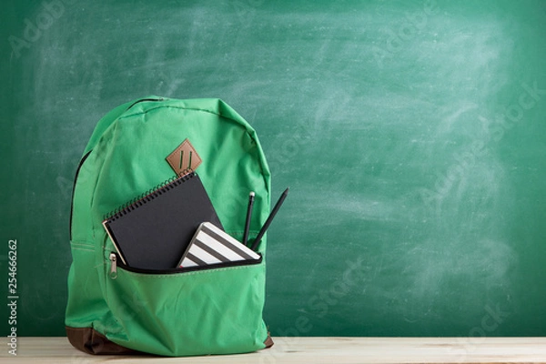 Fototapeta green backpack, black notebooks and pencils on the background of the blackboard