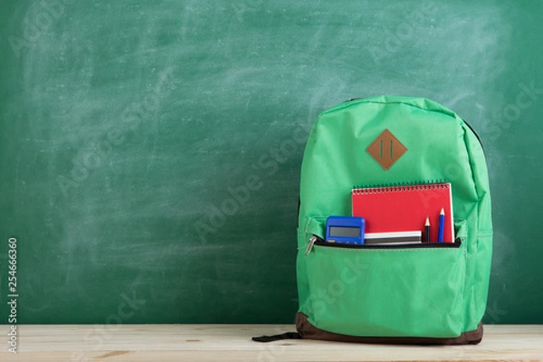 Fototapeta green backpack, calculator and notebook on the background of the blackboard