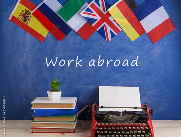 Fototapeta typewriter, flags of Spain, France, Great Britain, books and other countries and blackboard with text "Work abroad"