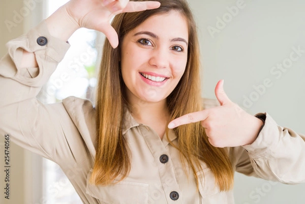 Fototapeta Beautiful young woman at home smiling making frame with hands and fingers with happy face. Creativity and photography concept.