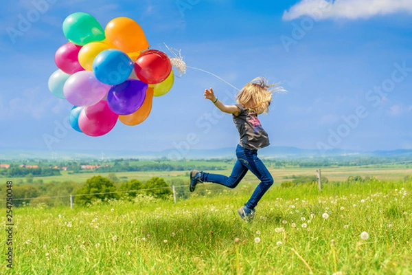 Obraz Glückliches Mädchen spring mit vielen bunten Luftballons über eine grüne Wiese