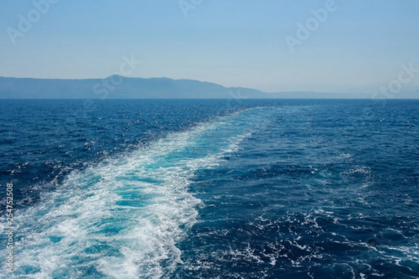 Fototapeta Island silhouette in the background. View from a boat with long path of waves from a boat. Deep dark blue water. Mediterranean Sea.