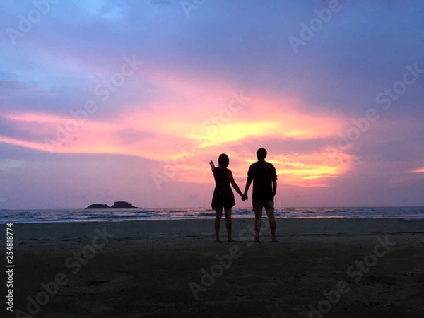 Obraz Couple hold each other hand at the beach under sunset. What a perfect moment under the sunset sky!