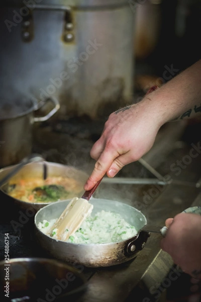 Obraz chef cooking in kitchen, stirring risotto in pan