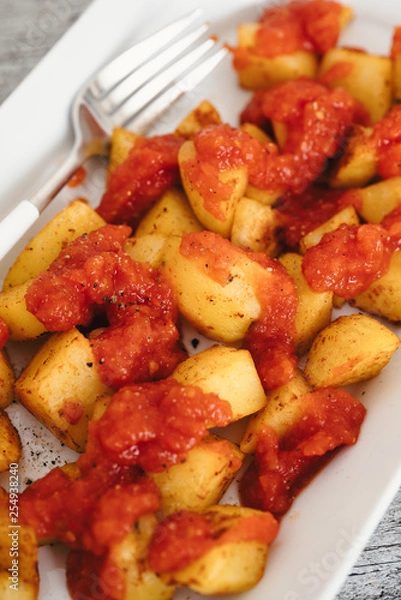 Fototapeta Papas Bravas, deep fried potato cubes typically served as tapas in Madrid, Spain with spicy mojo rojo, a red hot sauce made of tomatoes, bell peppers, onions and chili on white plate and wooden table