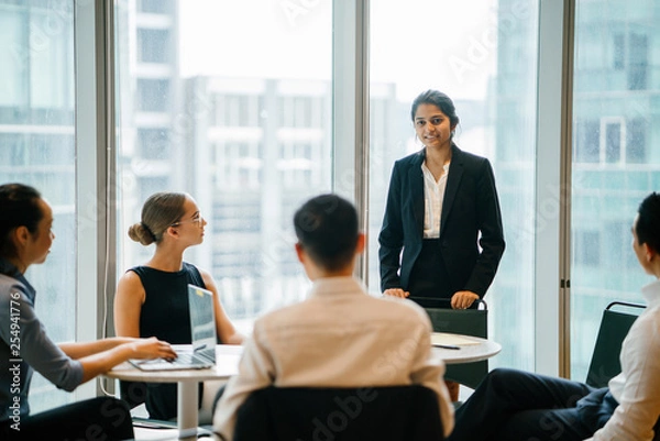 Fototapeta An Asian Indian businesswoman is having a conversation with her colleagues in a conference room and looking forward for their project. She's wearing a black blazer and white blouse with a black skirt.