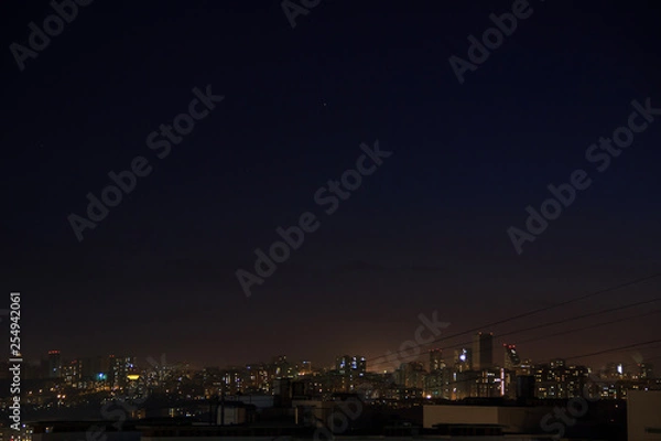 Fototapeta City skyline at night. Amazing panoramic view of modern city.Construction site with cranes on new residential areas.Stars on dark blue sky