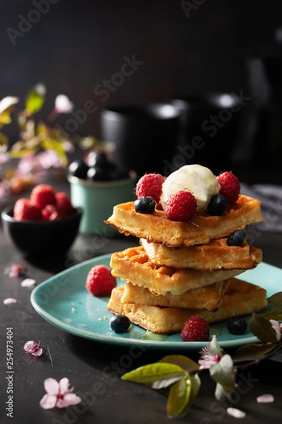 Obraz Freshly baked waffles with raspberries, berries, honey and coffee for breakfast or brunch on a dark background with copy space. Homemade Dessert concept.