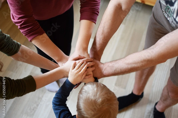Obraz Stack of family people hands - father with children on light brown wooden texture laminate floor background indoors, little boy in middle. Family business, teamwork and unity concept.