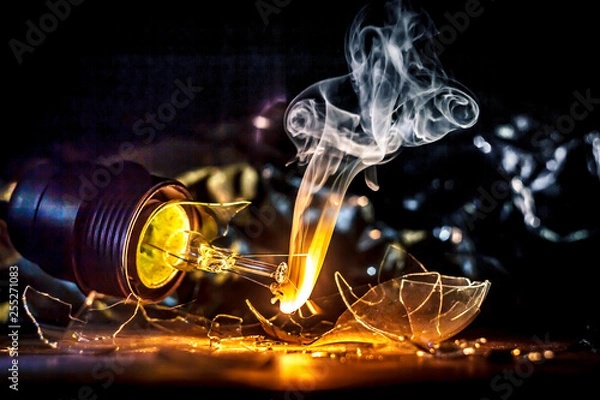 Fototapeta Amazing explosion of burning light bulb with splinters of broken glass and smoke on isolate black background. Сoncept of creative art illustrations of tungsten filament combustion in contact with air