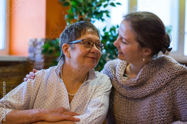 Fototapeta A woman and her mom are cute looking at each other in a cafe restaurant. They have not seen each other for a long time and they are together again.