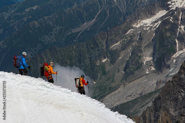 Fototapeta A group of three-person climbers continuing their descent along a ridge against the backdrop of mountains and clouds. Team work concept