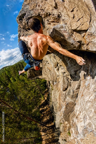Fototapeta Extreme climber hangs on a rock without a rope free solo. Vertical panorama