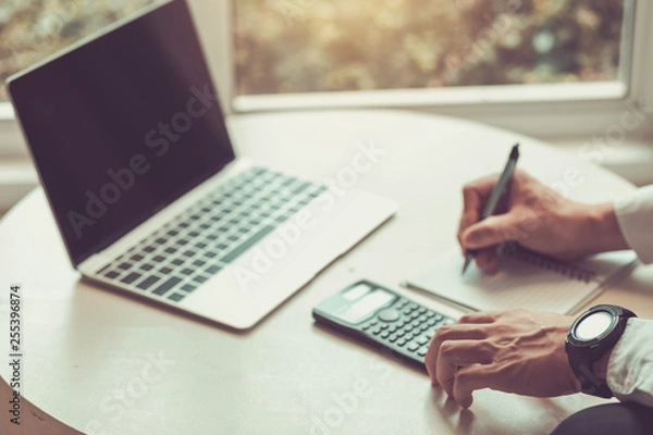 Fototapeta Man using calculator and writing make note with calculate about cost.