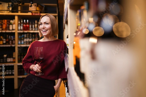 Fototapeta Image of woman with wine glass in store on background of shelves