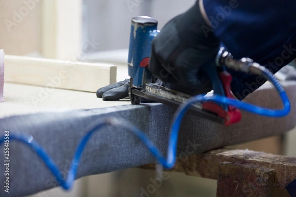 Fototapeta Closeup of a young man in a furniture factory who puts together one part of the sofa with a stapler