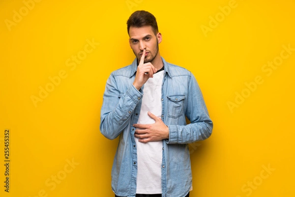 Obraz Handsome man over yellow wall showing a sign of silence gesture putting finger in mouth