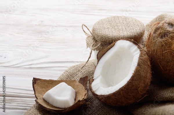 Fototapeta Coconut shell with meat on hemp sackcloth on white wooden kitchen table