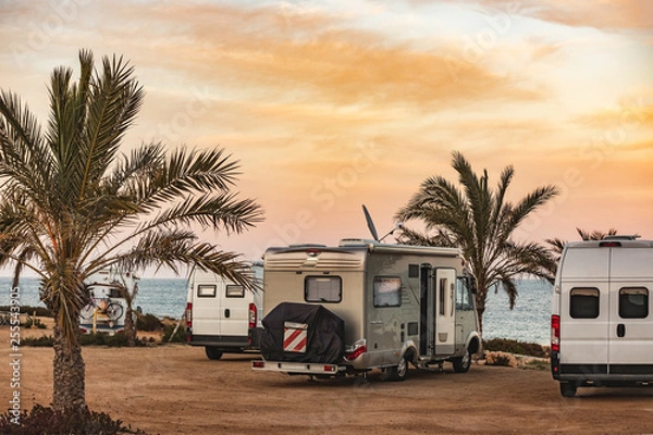 Fototapeta Motorhome making wild camp on the beach at a beautiful sunset or sunrise with mountains in the background. Caravan parked on the beach in front of the blue sea in a beautiful place of wild nature