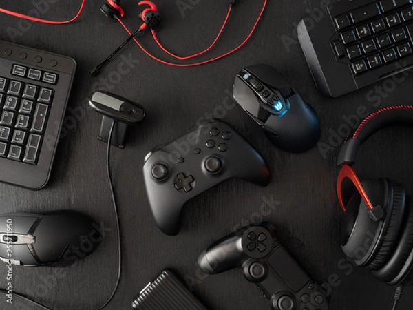 Fototapeta gamer workspace concept, top view a gaming gear, mouse, keyboard, joystick, headset, mobile joystick, in ear headphone and mouse pad on black table background with copy space.