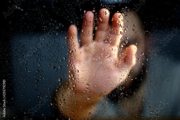 Fototapeta Male hand palm silhouette through the window with raindrops reaching for the glass. A request for help, depression blurred bokeh background