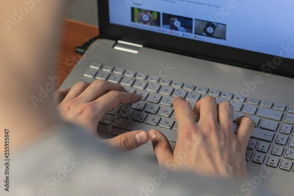 Obraz A young man typing on a laptop keyboard. Rear view, soft focus. Hard work at home