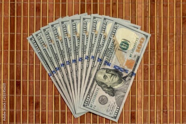 Obraz The stack is 100 dollar bills USD spread out like a fan, on a wooden background.