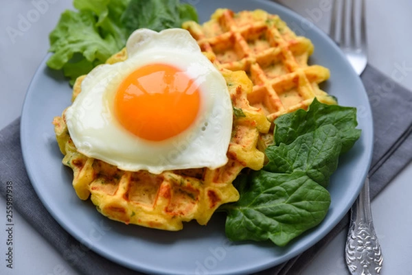 Fototapeta Spinach cheese waffles with fried egg on gray wooden background. Selective focus.
