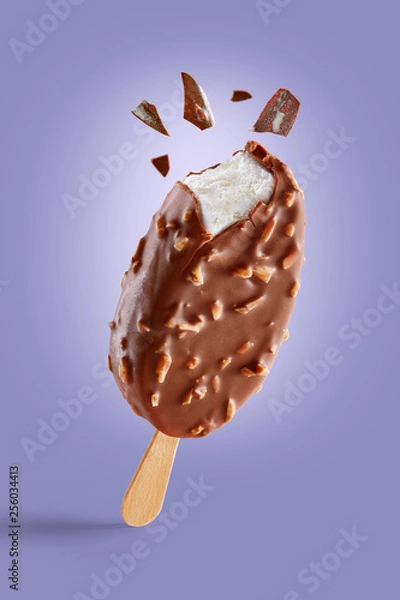 Fototapeta Chocolate covered ice cream with nuts on a purple background  bitten on top with chocolate bits. Taste explosion