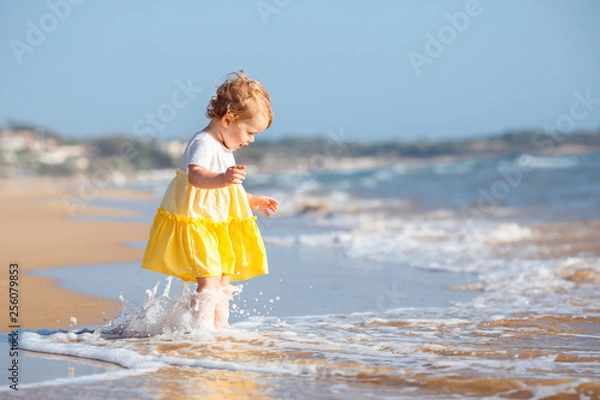 Fototapeta Adorable toddler girl wearing yellow dress splashing in ocean waves