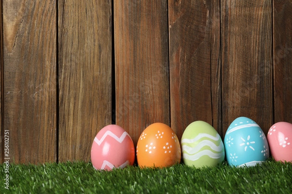 Obraz Colorful painted Easter eggs on green grass against wooden background, space for text
