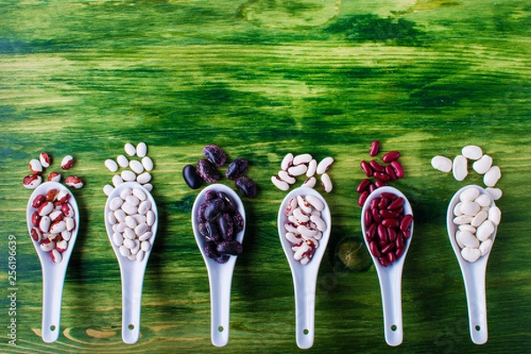 Fototapeta various dried legumes in wooden spoons on green background