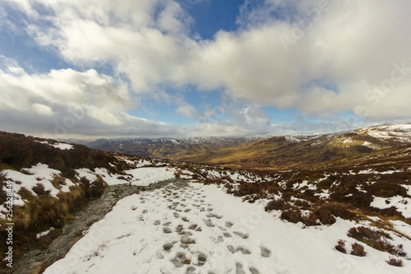 Fototapeta A snowy mountain path under a majestic blue sky and white clouds