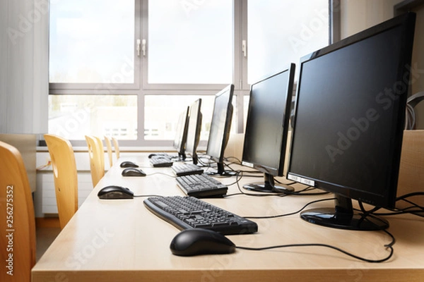 Fototapeta Empty computer room with monitors and keyboards in a row for pupils and students in a school computer lab