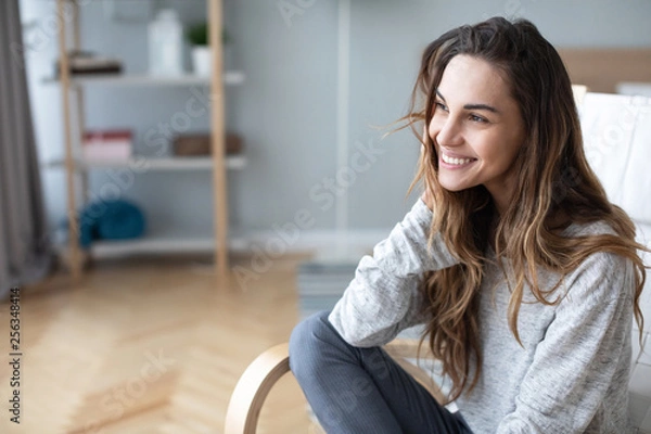 Obraz Happy woman posing sitting on a sofa in the living room at home.