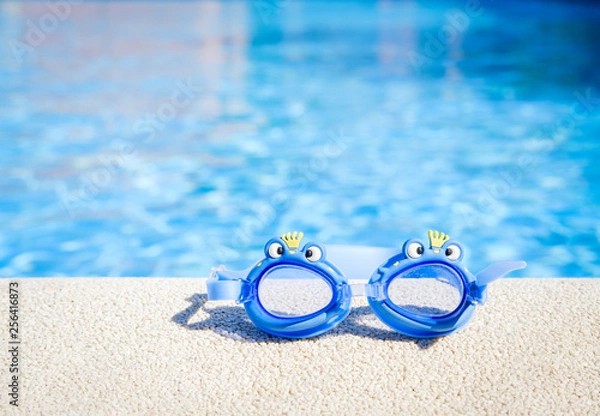 Obraz Closeup view of a boy blue swimming goggles on the pool edge with a big blue water copy space during a sunny summer day