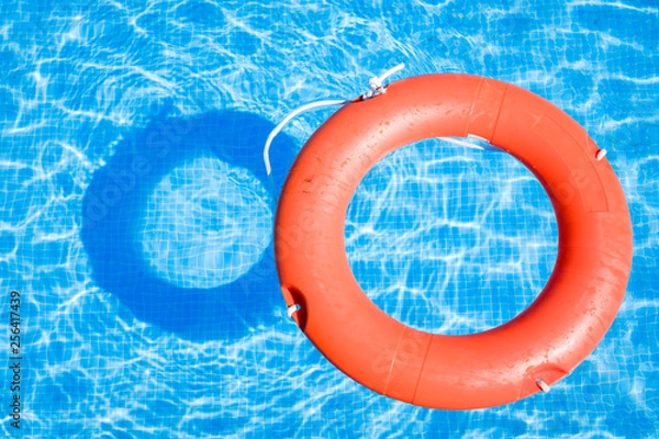 Obraz Closeup view of a red ring life buoy and its shadow floating on the blue water of the swimming pool during a sunny summer day