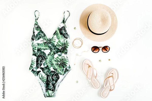 Fototapeta Woman's beach accessories: swimsuit with tropical print, rattan bag, straw hat on white background. Summer background. Flat lay, top view.