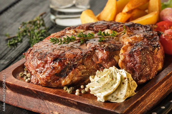 Obraz Ribeye steak with potatoes, onions and baked cherry tomatoes. Juicy steak with flavored butter