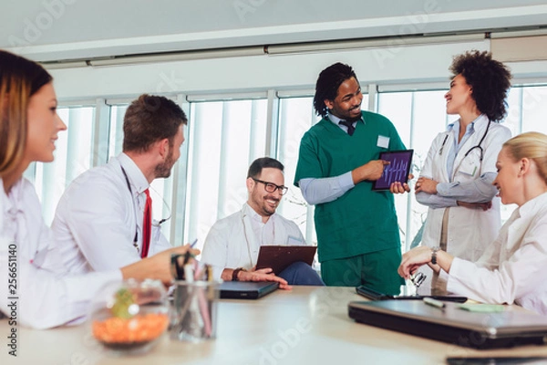 Fototapeta Medical team sitting and discussing at the table in the office, using digital tablet.